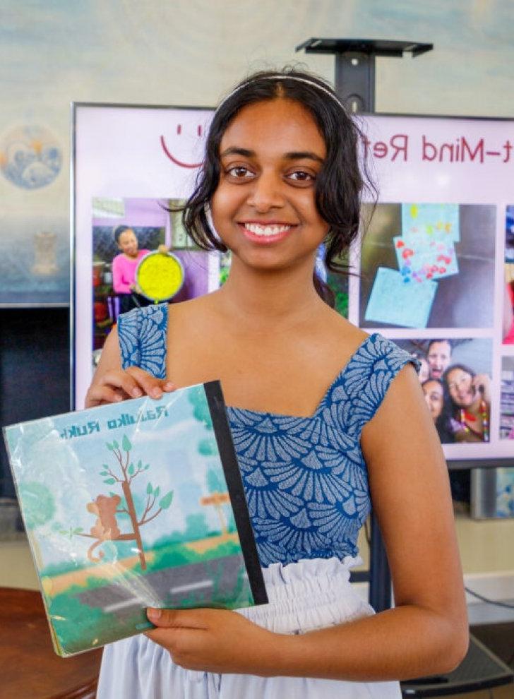 Pratya Poosala holds up a children's book she created in Nepali with an illustration of a monkey on a tree.